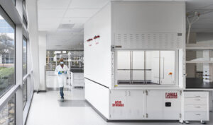 A spacious laboratory featuring fume hoods and casework, with large windows allowing natural light