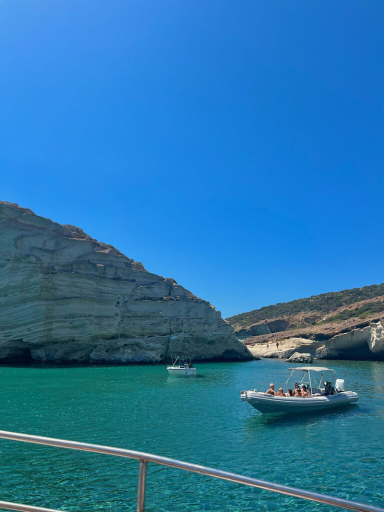 An island view from Greece showing clear blue water, a boat, and dramatic cliffs