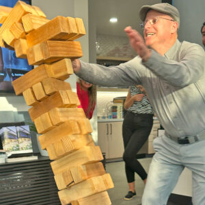 A man in gray smiles as a Jenga tower comes crashing down