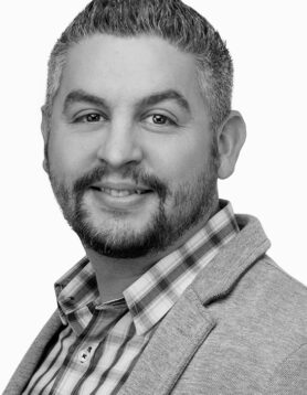 Nic Goddard, Designer III, smiling in black and white professional headshot